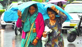Women cover themselves with a plastic sheet during heavy rain in Dehradun on Friday.