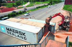An excavator fills sand into shipping containers placed by security forces as roadblocks on a street in Islamabad on Wednesday, ahead of proposed a protest march by opposition parties on I-Day
