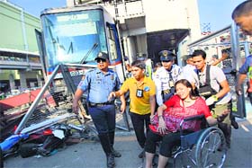 Rescue workers assist an injured passenger on a wheelchair as they alight from a coach of the Metro Rail Transit after it derailed in Pasay city on Wednesday