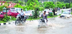 Motorcyclists pass through a waterlogged road after heavy rain in Jammu on Saturday. Tribune photo: Anand Sharma