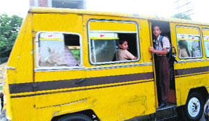 A schoolboy stands at the door of a moving bus in violation of safety norms in Amritsar.
