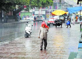 Caught unaware: A man covers his head with a plastic sheet as rain lashes the Kashmir valley on Wednesday