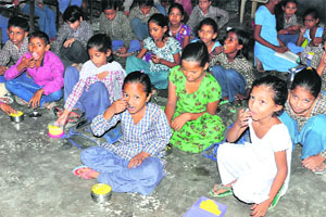 Students eat on the floor at a school.