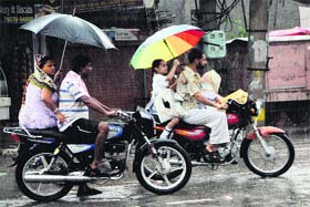 Youngsters carry umbrellas while riding motorcycles to protect themselves from rains in Amritsar on Thursday