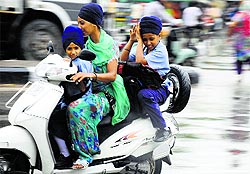 A woman ferries her children home on a scooter as it rains in Ludhiana on Thursday