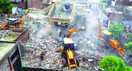 Earthmoving machines raze illegal structures; and (below) a resident breaks down at Pavittar Nagar, Ludhiana, on Saturday.