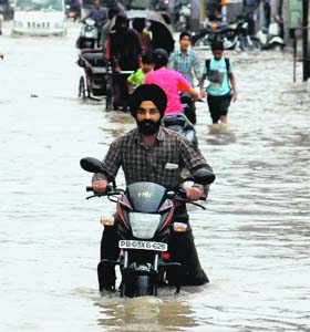 Commuters make their way through a road filled with water near Teachers Home in Bathinda on Monday