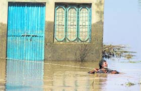 Tough time: A man uses a rope while he wades through a flooded field in front of his house following heavy rain in Pindi Bhattian, Punjab, on Tuesday