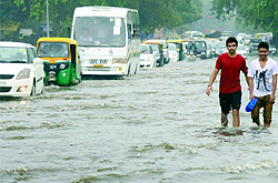 People face a tough time to cross a water-logged road near Connaught Place after heavy rain in New Delhi on Thursday