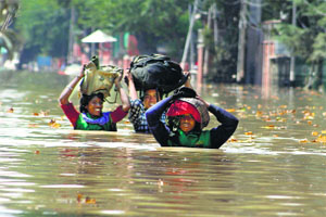 Migrant workers hold their bags on their heads as they wade through a flooded road in Srinagar.