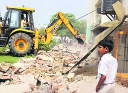 An earthmover demolishes an extended area of a house; a resident argues with the police for removing encroachments without warning.