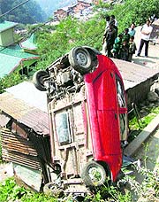 Onlookers gather near the overturned car near Sabzi Mandi in Shimla on Monday.