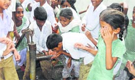 Due to lack of drinking water facilities, schoolchildren queue up at a hand-pump