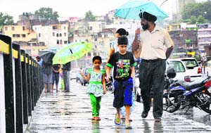 A family walks on the Tawi Bridge during rain in Jammu.