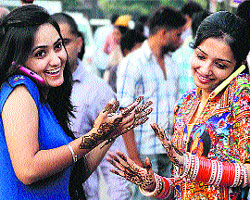 Young girls make calls on their cell phones after getting henna applied on their hands a day ahead of Karva Chauth in Jalandhar on Friday.