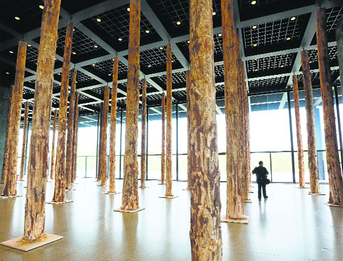 A man walks between tree trunk columns that are part of the installation Sticks and Stones  An Intervention by British architect David Chipperfield in the upper glass hall of the New National Gallery in Berlin.