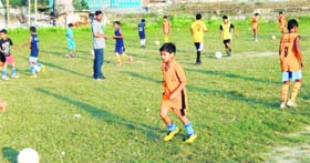 Children learn football techniques, while coach Munish Panjloo observes them at the Municpal Ground in Kangra