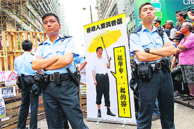 Policemen stand beside a cutout made by protesters featuring a manipulated photo of Chinese President Xi Jinping holding an yellow umbrella, at Mongkok on Sunday