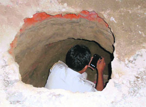 A cop takes pictures of the tunnel dug by thieves.