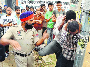 A policeman slaps two students from Rwanda who were allegedly caught stealing a cash box from a store in Jalandhar on Tuesday.
