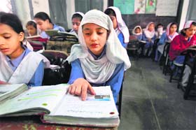 A girl reads a book while attending her daily class with others at a government school in Peshawar