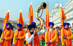 A Sikh devotee plays a musical instrument as he walks with the Panj Pyaras holding flags during a nagar kirtan ahead of the martyrdom anniversary of Guru Teg Bahadur at the Golden Temple in Amritsar on Saturday