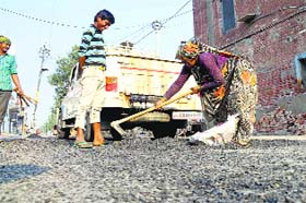 Workers collect material that came off from a repaired stretch of road in Rajpura on Monday