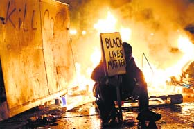 A demonstrator sits in front of a street fire during a demonstration following the grand jury decision in the shooting of Michael Brown, in Oakland on Tuesday