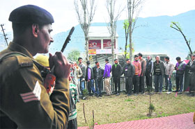 A security man keeps vigil as voters queue up outside a polling station during the first phase of elections in Ramban district on Tuesday