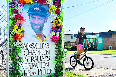 A boy rides his bicycle next to a portrait of the late Phillip Hughes in his hometown Macksville on Saturday. 